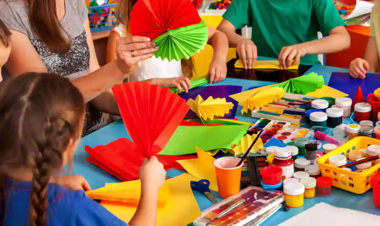 Children participating in a craft program showing a table with paints, construction paper